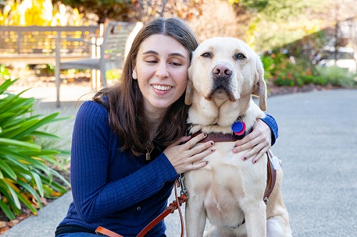 Megan crouches down on a path to hug her yellow Lab guide dog.