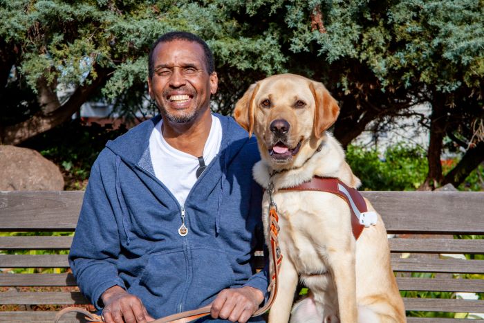 Willie sits on a bench next to his guide dog, Niner, a yellow Lab. 